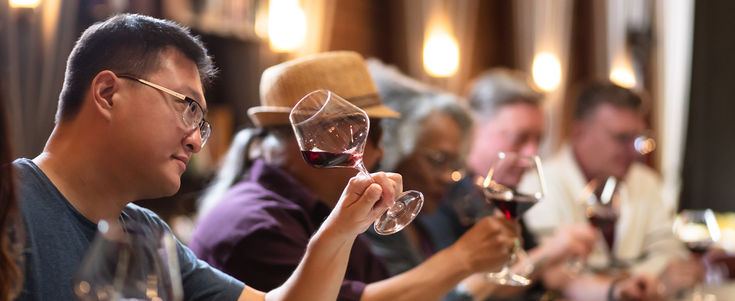 Group of people at a wine tasting event tilting glasses of red wine to examine color and clarity