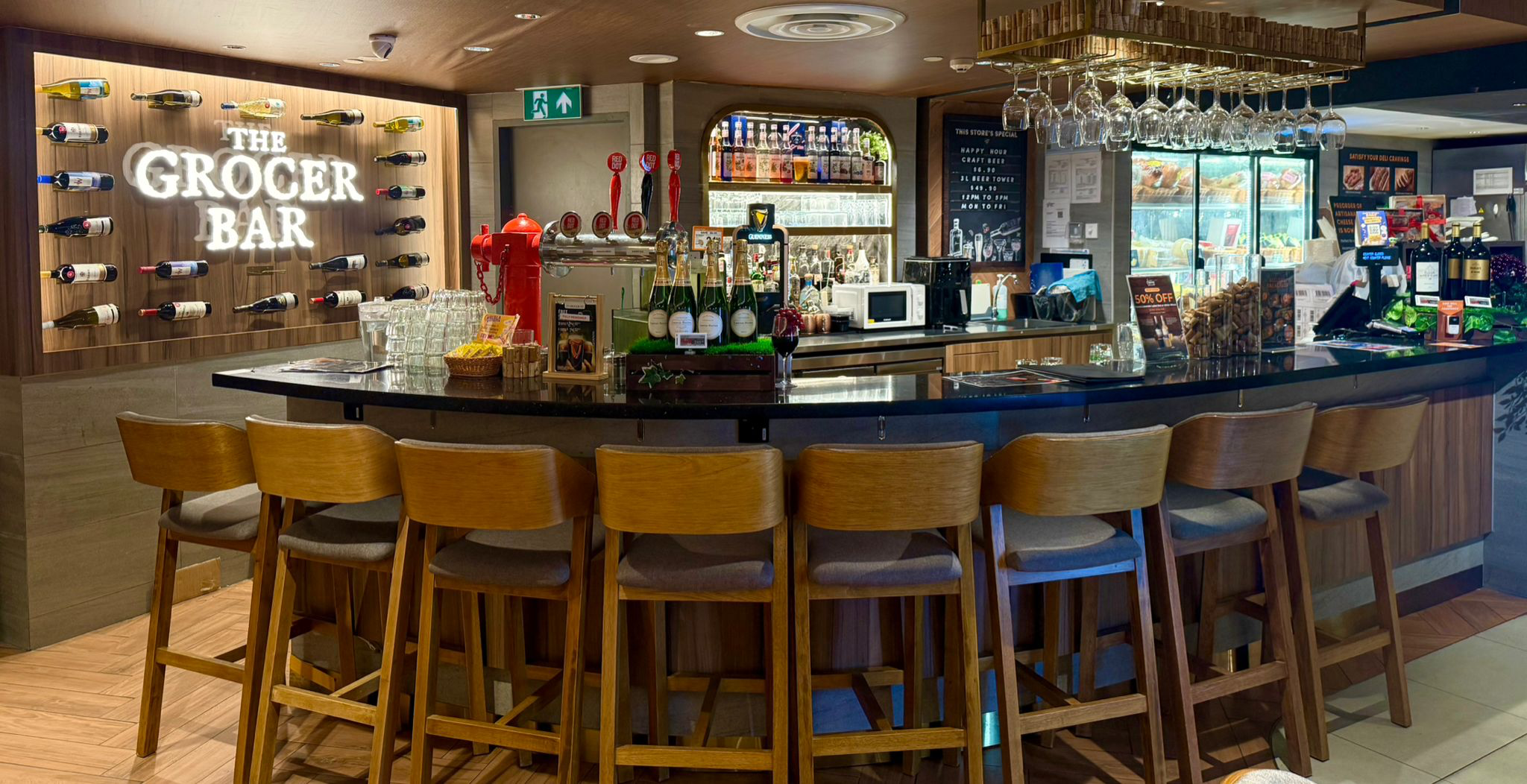 The Grocer Bar at FairPrice Finest Centrepoint with a curved wooden counter, wine displays and hanging glasses.