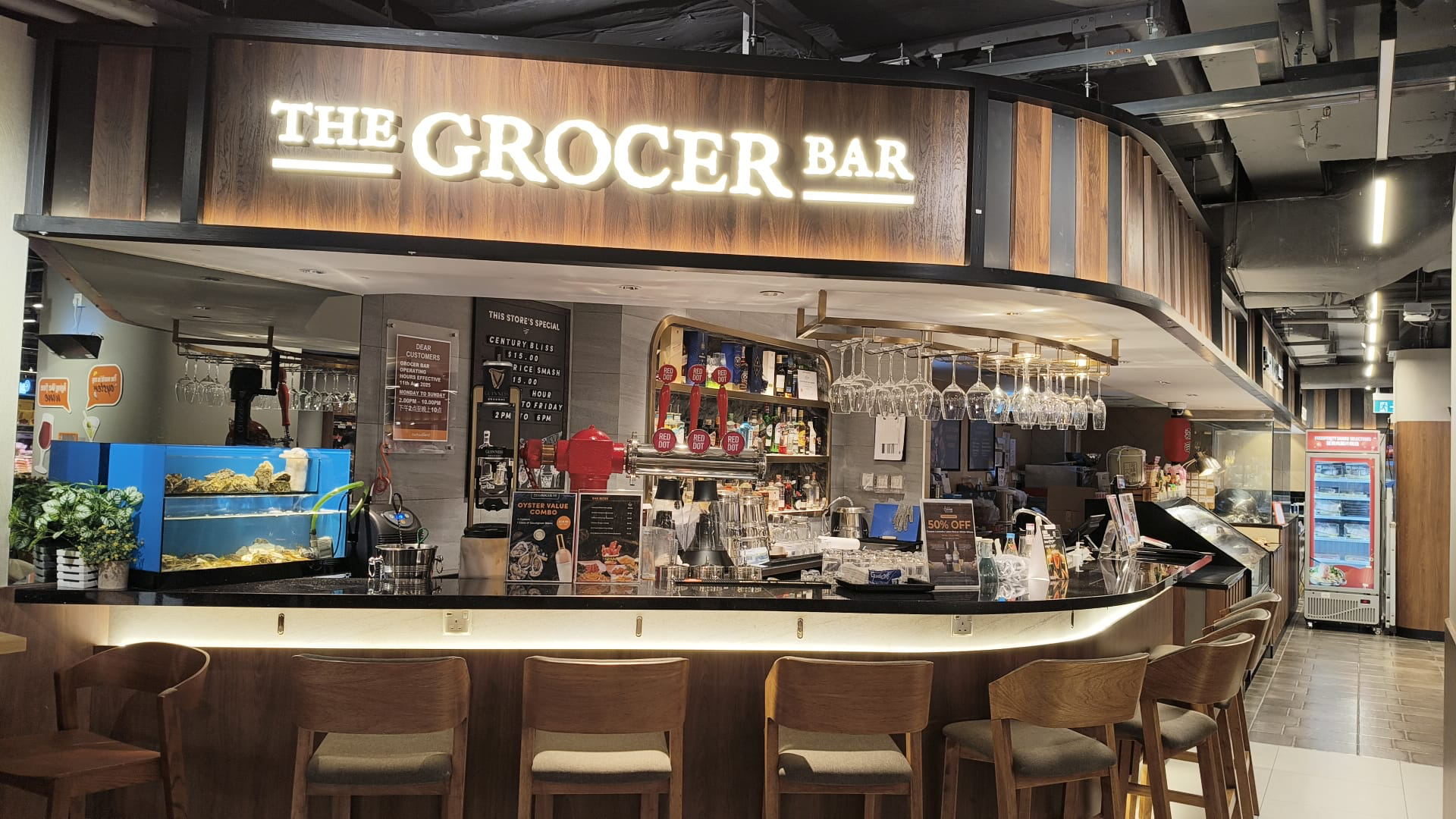 The Grocer Bar at FairPrice Finest Century Square with a curved wooden counter and matching barstools.